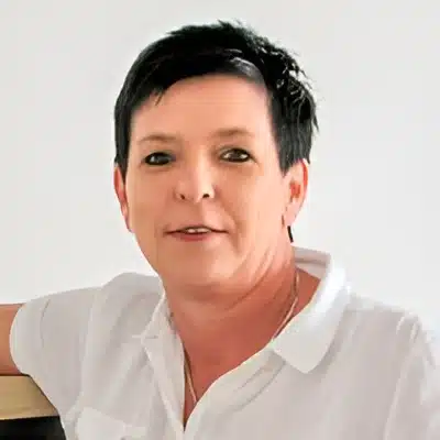 Stefanie Nelius Portrait einer Frau mit kurzen dunklen Haaren in weißer Bluse vor hellem Hintergrund.